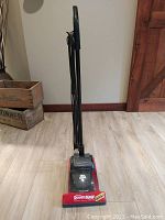 Front view of upright vacuum showing handle and base with 'RoomMate' label, cord wrapped on handle.