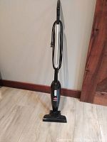 Bissell Magic Vac upright vacuum cleaner standing upright on a wooden floor, showing handle, cord, and base unit.