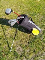 Junior golf club set with red shafts in black and yellow standing bag on grass.