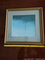 Front view of the framed Robert Bateman print showing the image of trees in snow with a gold-colored frame and a ruler for scale.