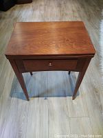 Closed wooden sewing table with drawer, polished medium wood tone and tapered legs