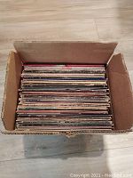 Top down view showing a filled cardboard box stacked with over 50 vinyl LP records with various visible spine labels.