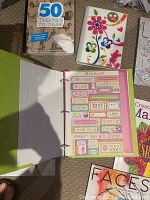 Open scrapbooking binder showing colorful stickers inside and various activity books including '50 Things To Draw'.