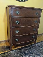 Front view of wooden highboy chest with four drawers showing oval metal handles and wood grain finish.