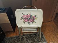 Front view of a single TV tray featuring white tray top and pink rose floral design, positioned on metal folding stand.