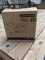 Box showing the Monitor Audio PRO-80 speaker with installation instructions printed on the front, placed on a wooden deck.