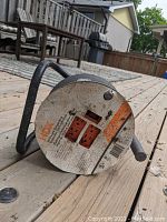 Close-up of the reel front plate showing two orange outlets, reset button, and product branding sticker worn with dirt and scuffs.