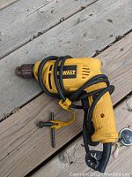 Photo of yellow Dewalt electric drill laid on wooden surface, power cord wrapped around handle.