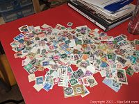 Photo of a large pile of assorted worldwide postage stamps scattered on a red table surface