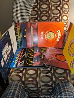 Full view of the 15 disco vinyl records and albums arranged on a patterned chair, showing colorful and varied album covers typical of the late 1970s disco era.