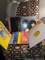 Overall view of 15 disco records and albums arranged on patterned chair showing colorful album covers and record sleeves.