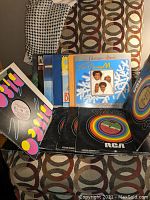 Photo showing 15 disco album covers and record sleeves arranged on patterned chair, illustrating the variety of vinyl records in the lot.