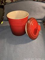 Red Le Creuset ceramic container with lid taken off, showing smooth white interior and brand embossing on the side.