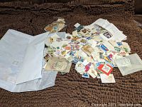 White envelope opened and content of hundreds of assorted used postage stamps spread on brown textured surface