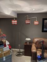 Full view of the floor lamp showing three hanging wooden slat lampshades, metal pole and base in a corner of room.