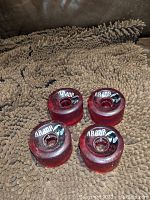 Four used red translucent skateboard wheels with white Arbor branding and black leaf graphic, placed on a textured brown surface.