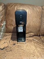 Front view of black SodaStream carbonation machine on brown couch with mat.
