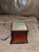 Closed box showing the ornate silver-tone metal inlay on the wooden top lid and the curved wooden base.