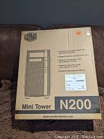 Photo of Cooler Master N200 Mini Tower cardboard box showing front with model name and features including mesh front panel, support for 240mm radiator and long graphics cards.