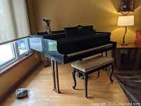 Full view of black Knabe baby grand piano with brass legs and bench in room