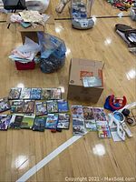 Wide shot showing row of Nintendo Wii games, Xbox games, some white Wii accessories and large cardboard box, also Wii Fit balance board, steering wheel accessories.