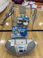 Clear Waterpik water flosser unit, Panasonic boombox, discman, and media items in plastic bag on gym floor.