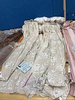 Set of 12 ecru brown floral drapes with gold rods inside each panel, shown folded and laid on a table.