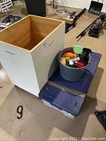 Wooden crate open top showing interior, next to bucket with cleaning supplies and two storage totes stacked