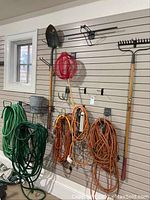 Wide shot showing garden hoses, extension cords, shovel, and rakes hanging on wall.