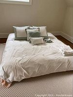 Full view of king size bed with cream-colored bedding, decorative pillows in cream/light green, and folded bedding on bed.