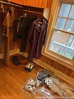 Full view of costumes hanging including leather pants, jackets, purple coat, and shoes along with accessories on floor.
