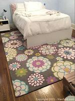 Area rug with colorful large floral patterns under a bed on a hardwood floor.