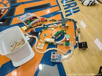 Overview of the wooden train layout with BRIO train track pieces, multiple wooden trains and cars, blocks, and several plastic totes.