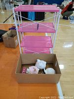 Pink folding rolling rack with four fabric shelves and some visible scratches. Box in front contains the three animal piggy banks: pig, sheep, and cow.