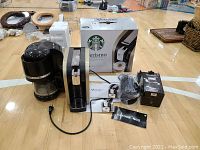 Starbucks Verismo coffee maker, KitchenAid drip coffee maker, Nespresso Aeroccino3 frother, manuals and original boxes shown on gym floor.