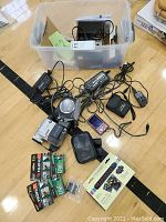 Photo showing multiple items including Sony handycams, cameras, chargers, batteries, Fujifilm digital videocassettes, Marshall's coloring system and binoculars.