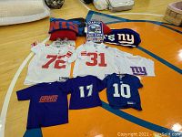 Photo showing assortment of NFL sports jerseys, mugs, pillows, and blankets arranged on surface.