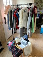 Full view of clothing rack with assorted sweaters, polo shirts, dress shirts, t-shirts, and tank tops along with folded clothing items and bags on the floor nearby