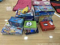 Photo showing a pile of 15 various board games including Life, Connect 4, Don't Wake Daddy, Battleship, Risk, and more stacked on gym floor.