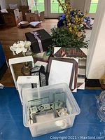 Full lot overview with items arranged on the floor including floral arrangements, boxes, frames, and scrapbook items.