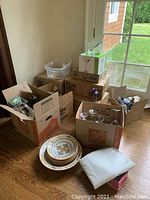 Multiple open boxes containing various glassware including martini glasses, whiskey glasses, wine glasses, shakers, and stacked decorative plates alongside boxed pasta bowl set.