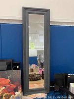 Full front view of tall rectangular mirror with gray-washed wood frame leaning against blue backdrop in a gym setting