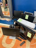 Five monitors and TV arranged in a cluster on the floor including three Dell monitors, one HP monitor, and one Insignia TV with remote.