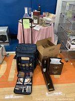 Full view of picnic backpack with glasses, cutlery, napkins, wooden wine holder, and boxes on gym floor.