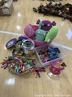 Wide image showing all toys together including plush dolls, plastic horse figurines, small plastic toys, and the pink container toy.