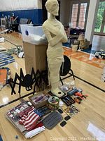 Freestanding mummy figure with pumpkin carving tools, spider yard decorations, and small American flags laid out on floor.