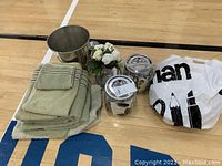 Full view of all items showing towels, two lidded jars, metal wash bin, and artificial flower arrangement on wooden surface