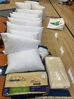 Row of white bed pillows with two packaged Tempur-Pedic pillows at front
