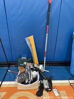 Assorted golf accessories displayed in basket and on floor: head covers, fabric bags, training aids, stretching pole.