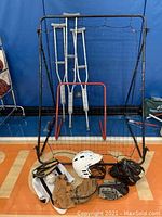 Full lot photo showing lacrosse net, crutches, baseball/softball gloves and helmet on gym floor